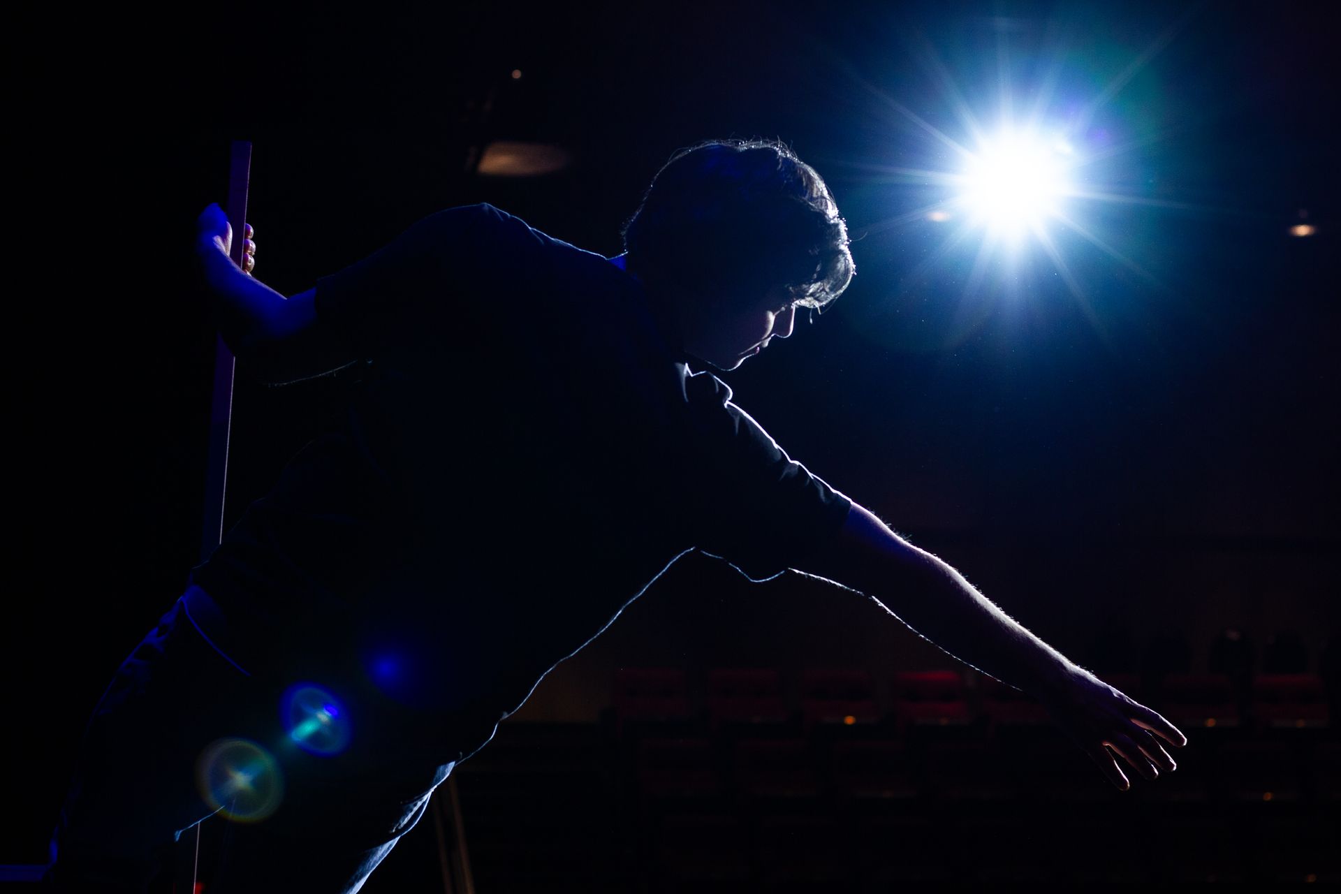 Silhouette of person reaching, illuminated by bright spotlight.