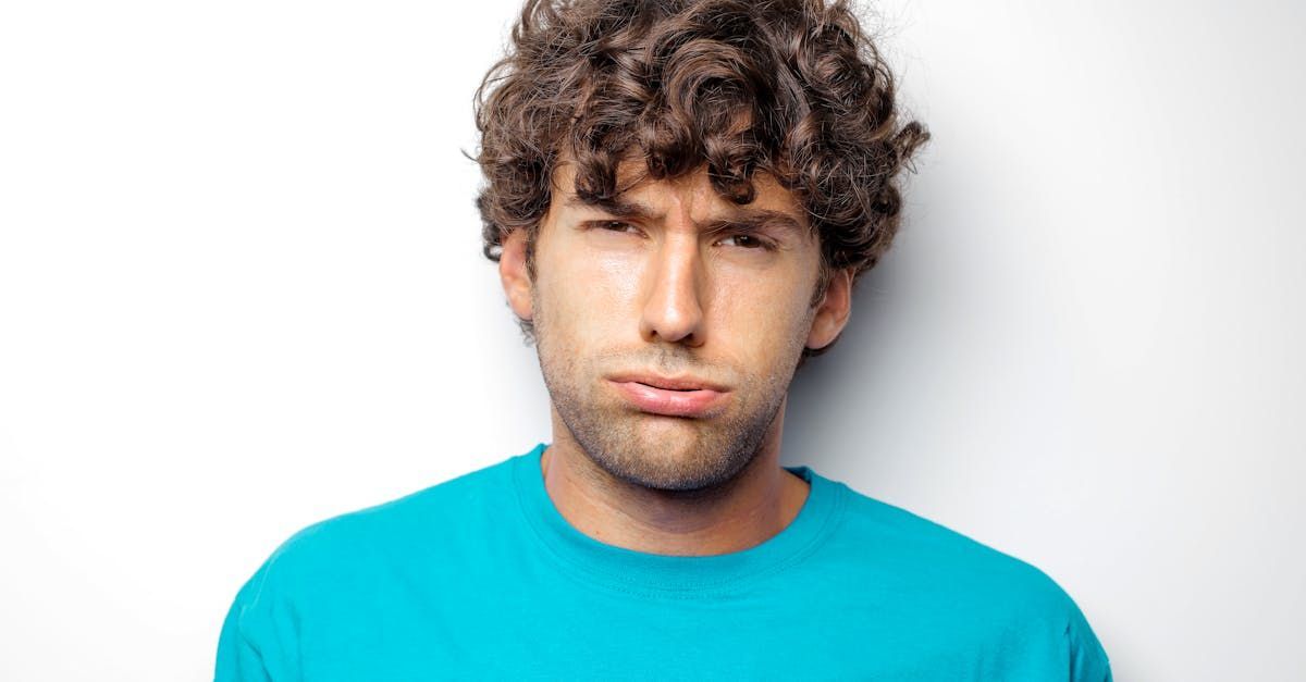 Man with curly brown hair and blue shirt looking doubtful, against a white background.