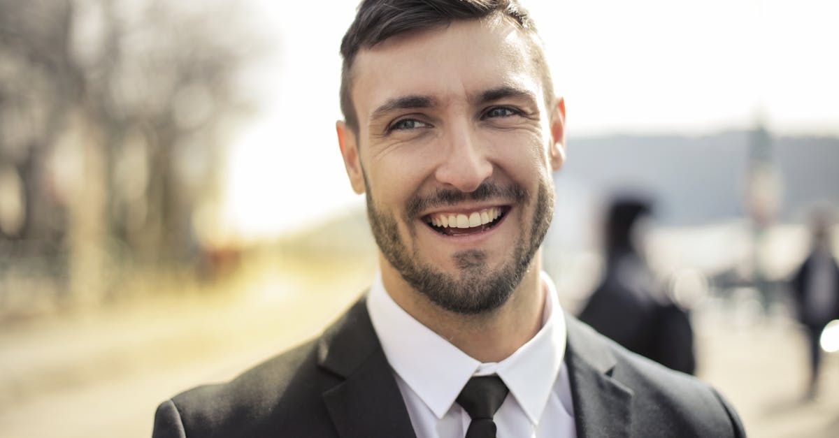 Man in suit smiles broadly outdoors, light background.