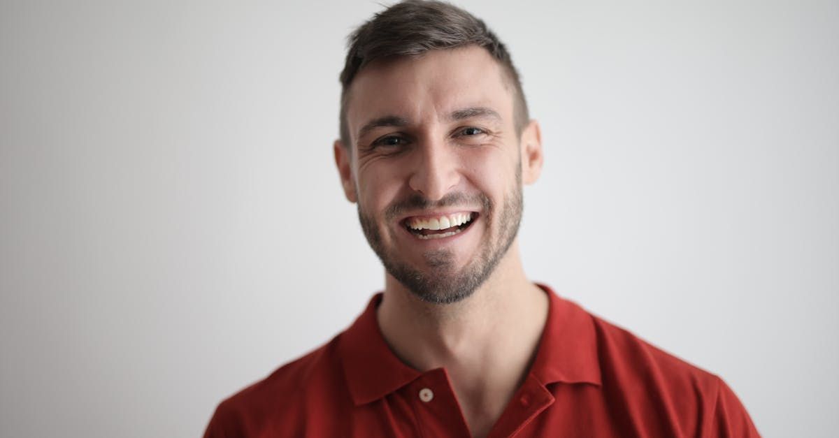 Man with a beard wearing a red polo shirt, smiling widely against a white background.