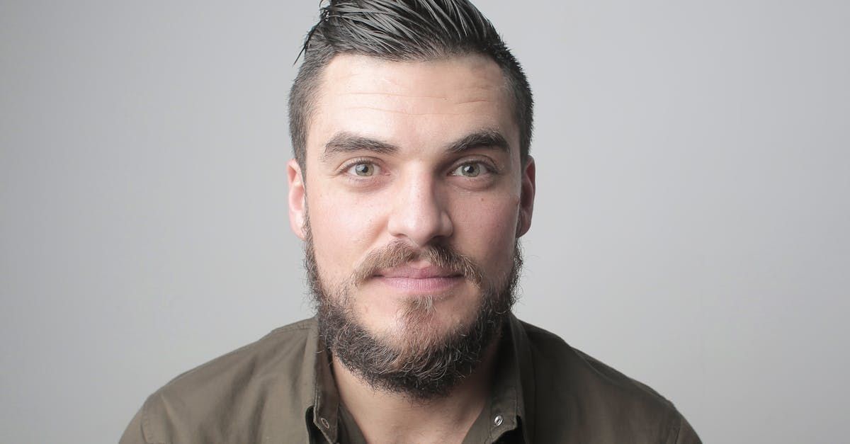 Man with a beard, dark hair, and a neutral expression against a gray background.