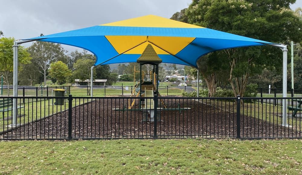 A Blue And Yellow Umbrella Is Covering A Playground In A Park — SPF Shades and Sails in Tweed Heads West, NSW