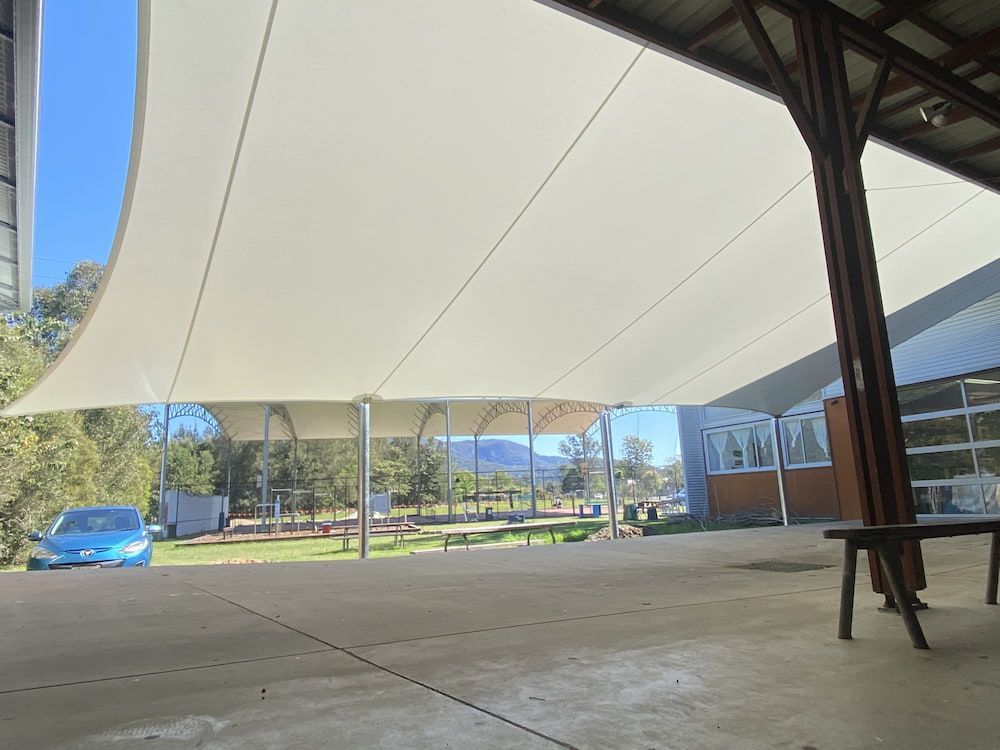 A Blue Car Is Parked Under A White Umbrella In Front Of A Building — SPF Shades and Sails in Byron Bay, NSW