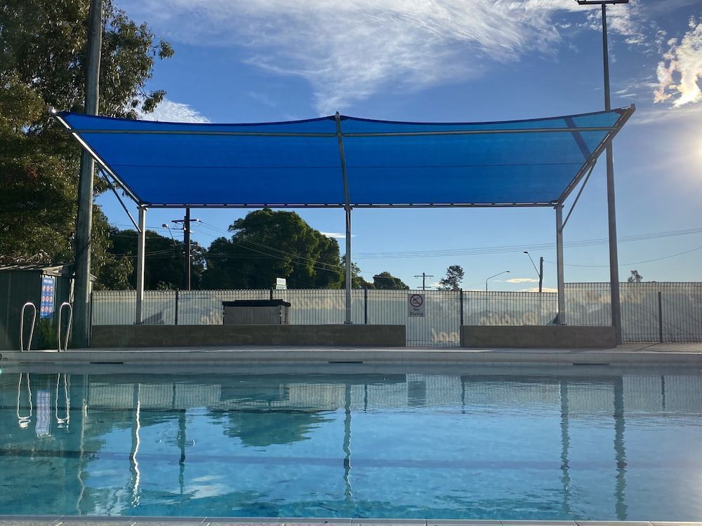A Swimming Pool With A Blue Umbrella Over It — SPF Shades and Sails in Tweed Heads, NSW