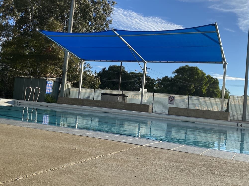 A Swimming Pool With A Blue Umbrella Over It — SPF Shades and Sails in Tweed Heads West, NSW