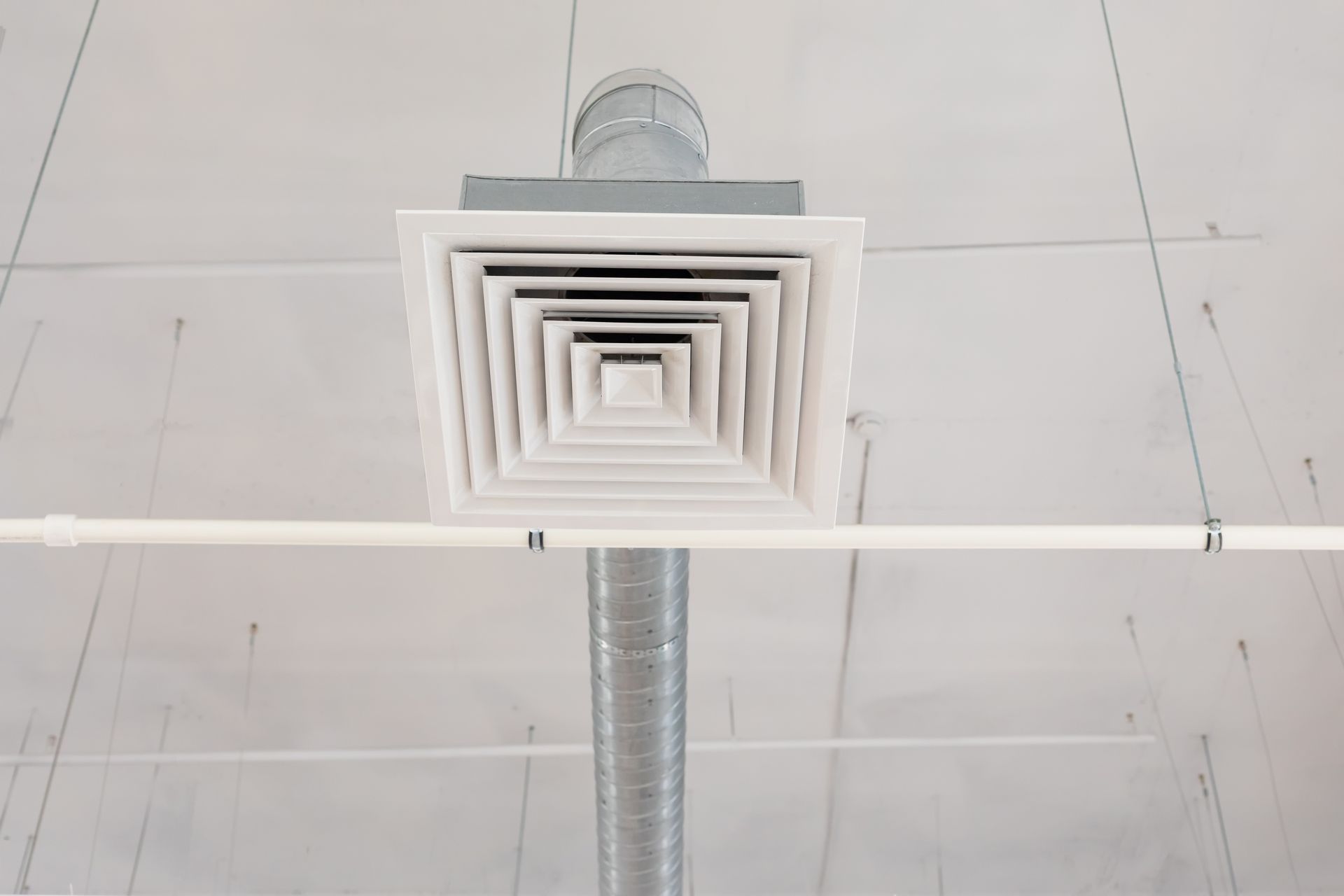 A square air vent is hanging from the ceiling of a building.