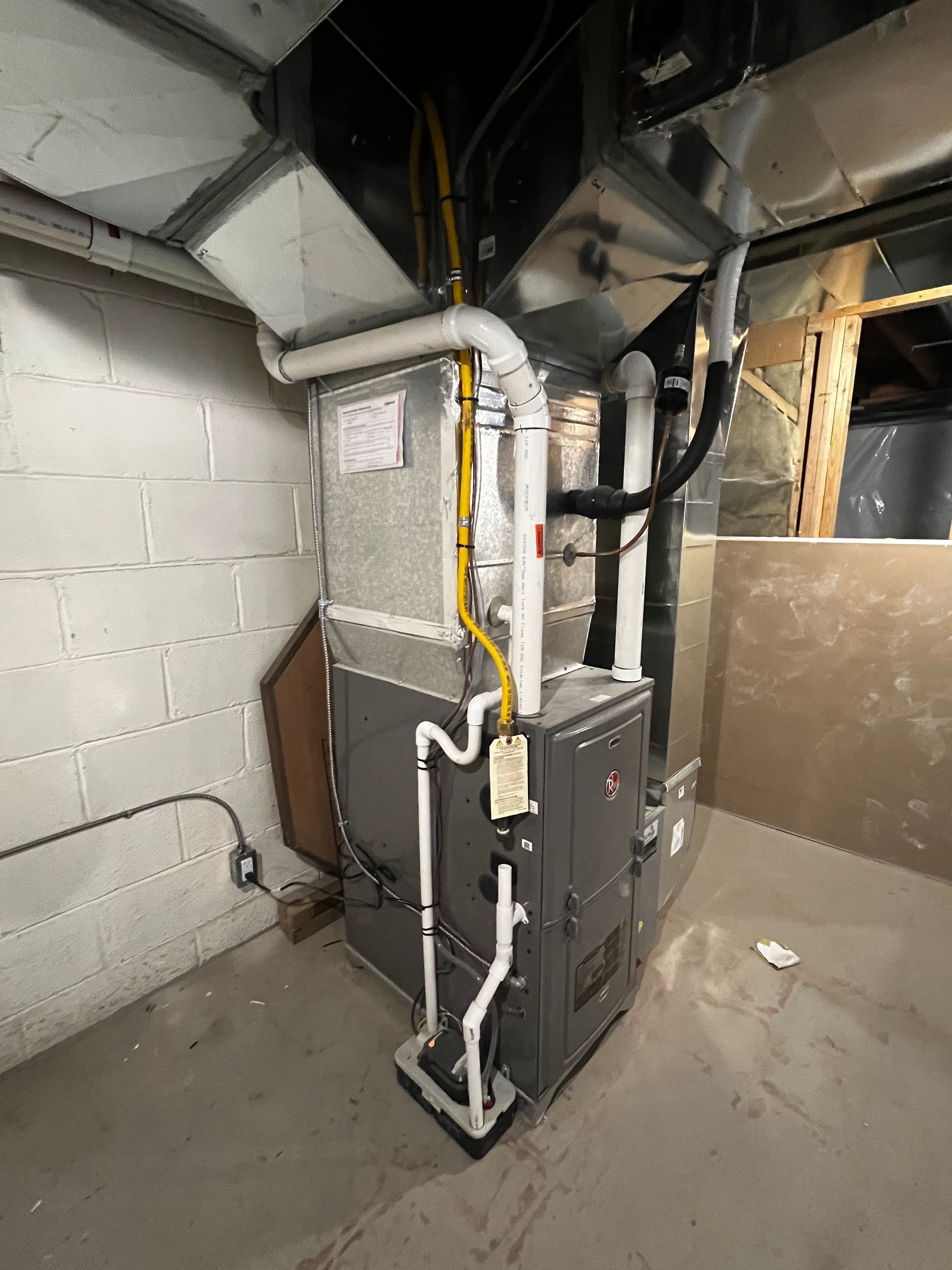 A gas furnace is sitting in a basement next to a brick wall.