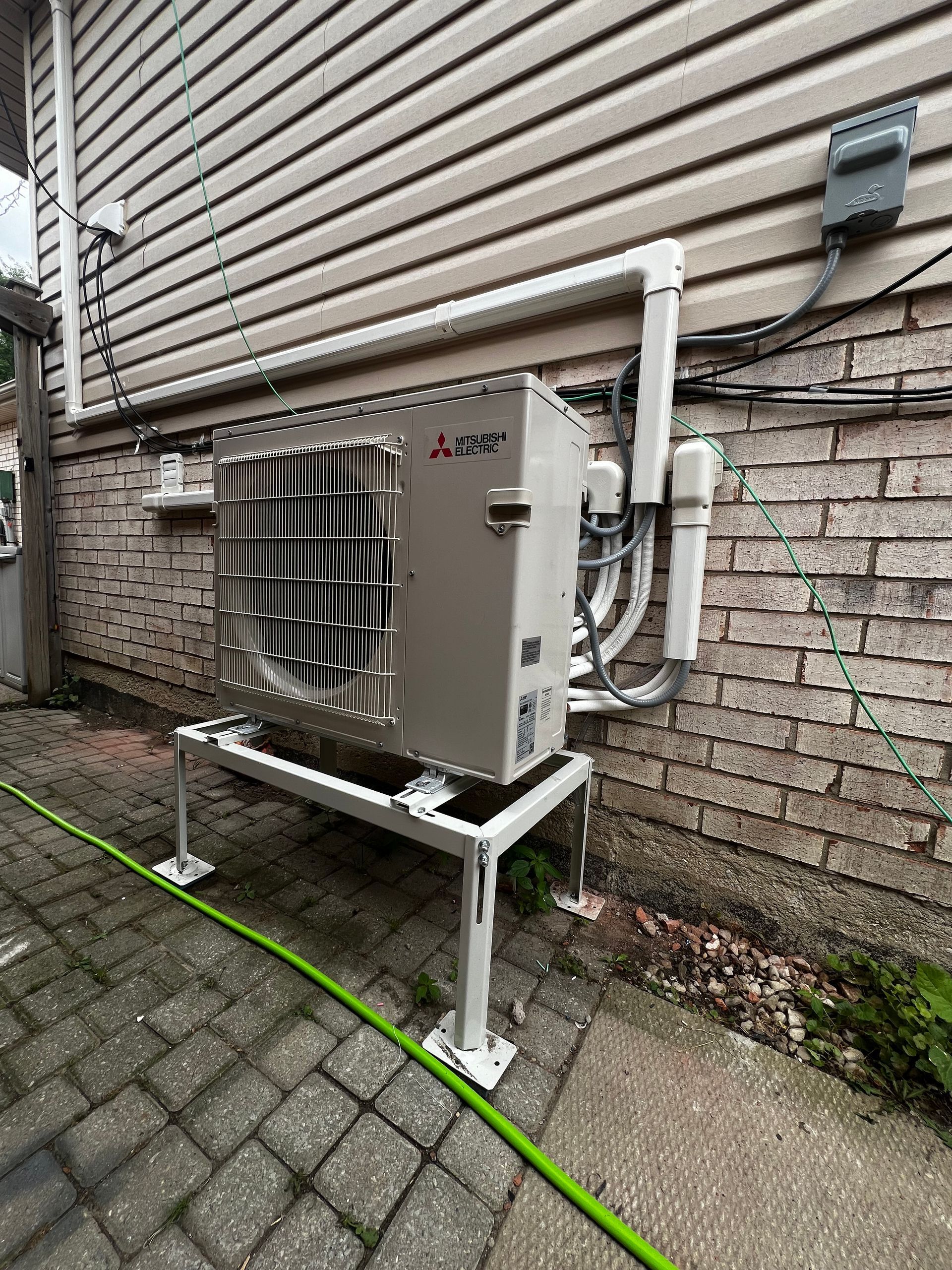 A white air conditioner is sitting on a stand on the side of a brick building.