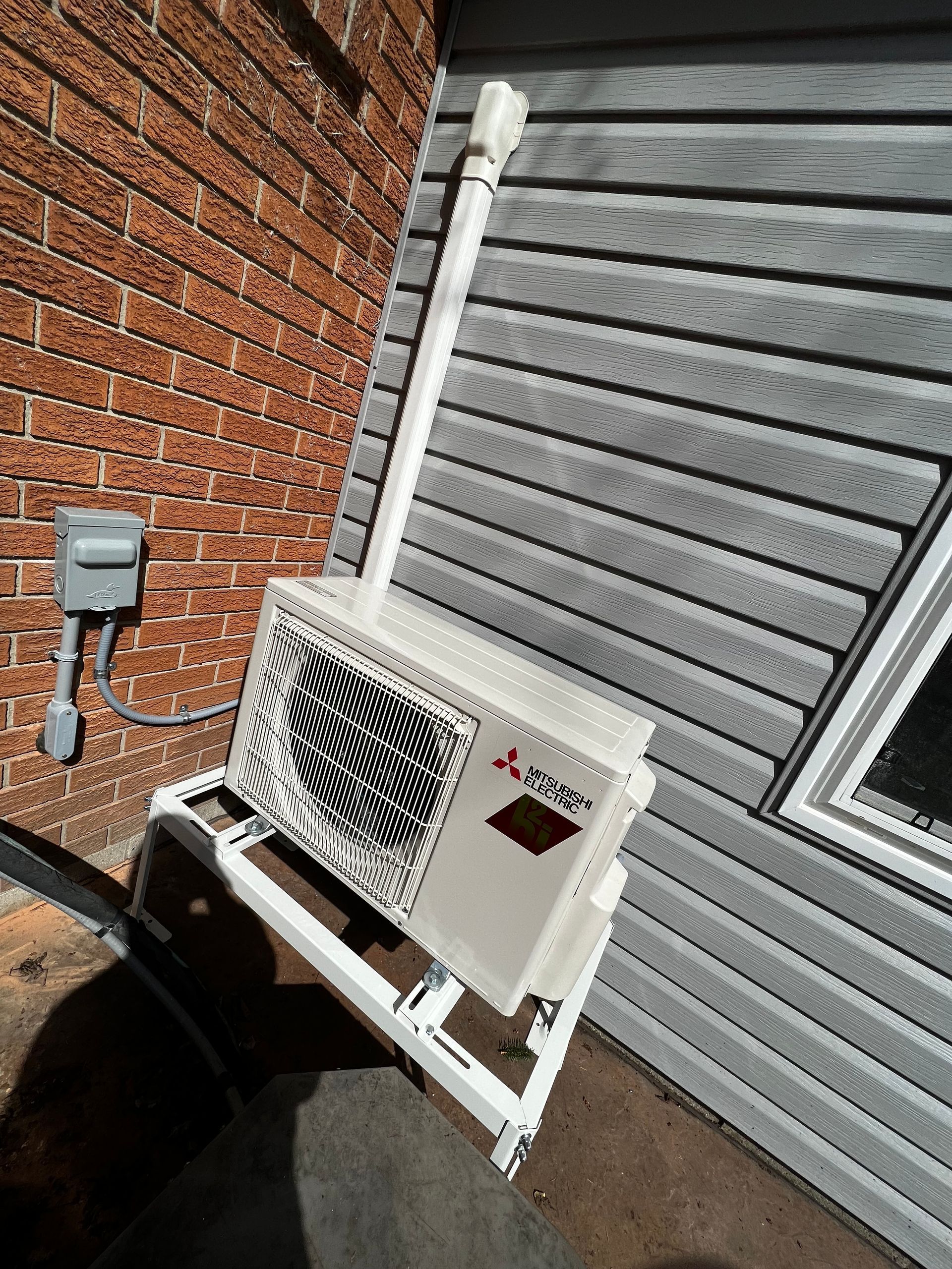 A white air conditioner is sitting on a white stand on the side of a house.