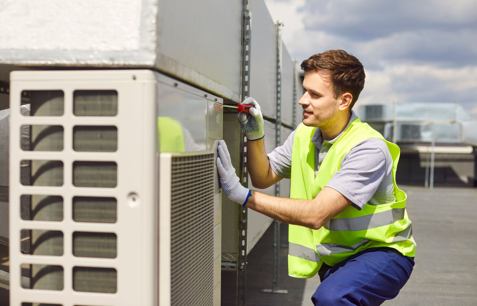 A man in a yellow vest is working on an air conditioner.