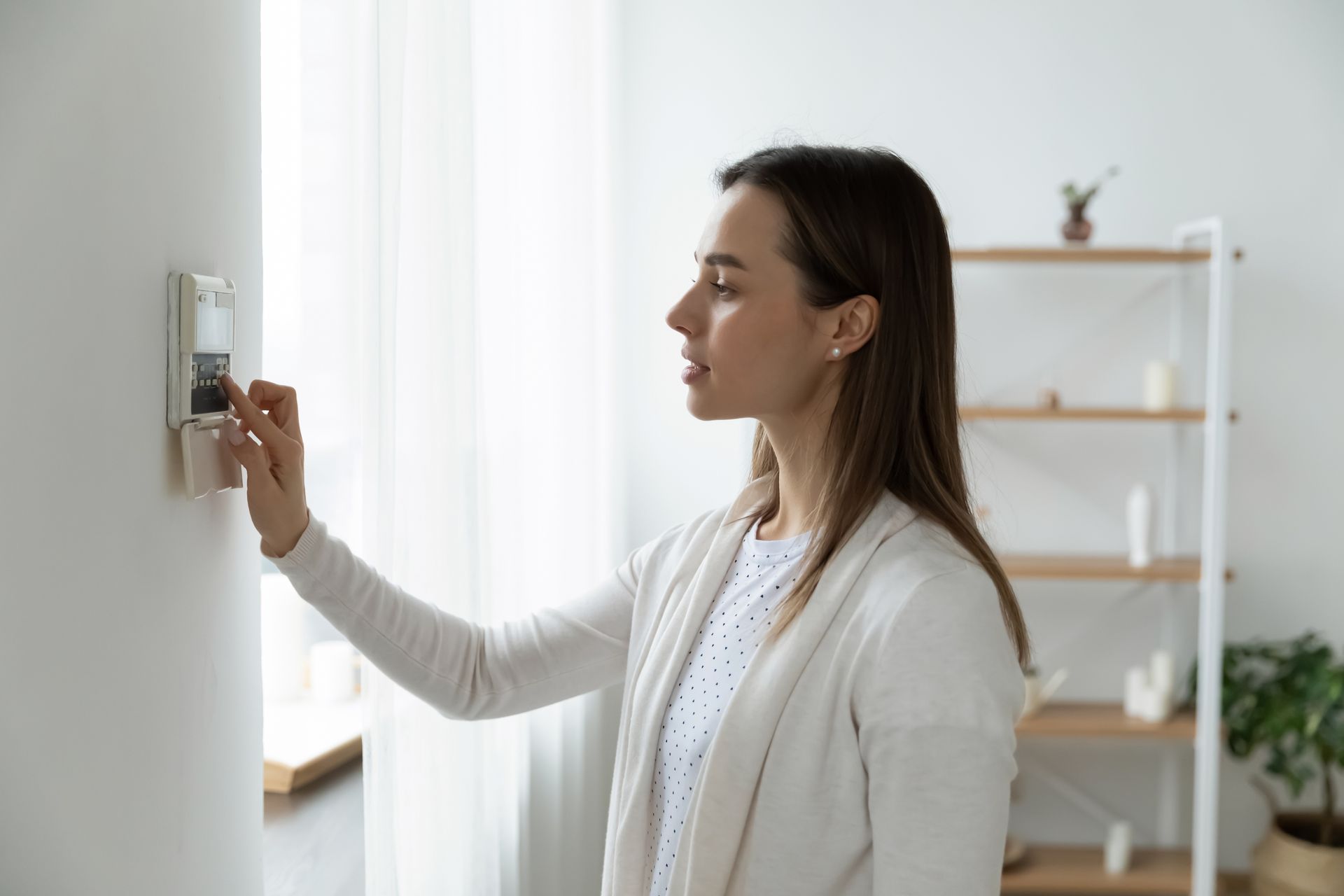 A woman is adjusting a thermostat in a living room.
