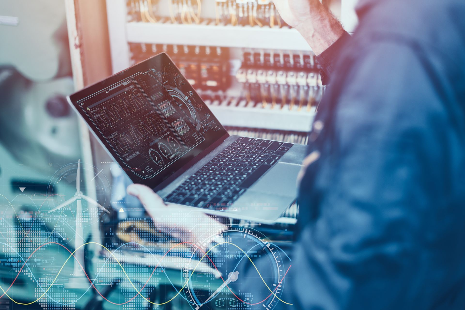 Una persona usa un computer portatile per ispezionare le apparecchiature elettriche all'interno di un ripostiglio. Indossa un'uniforme blu.