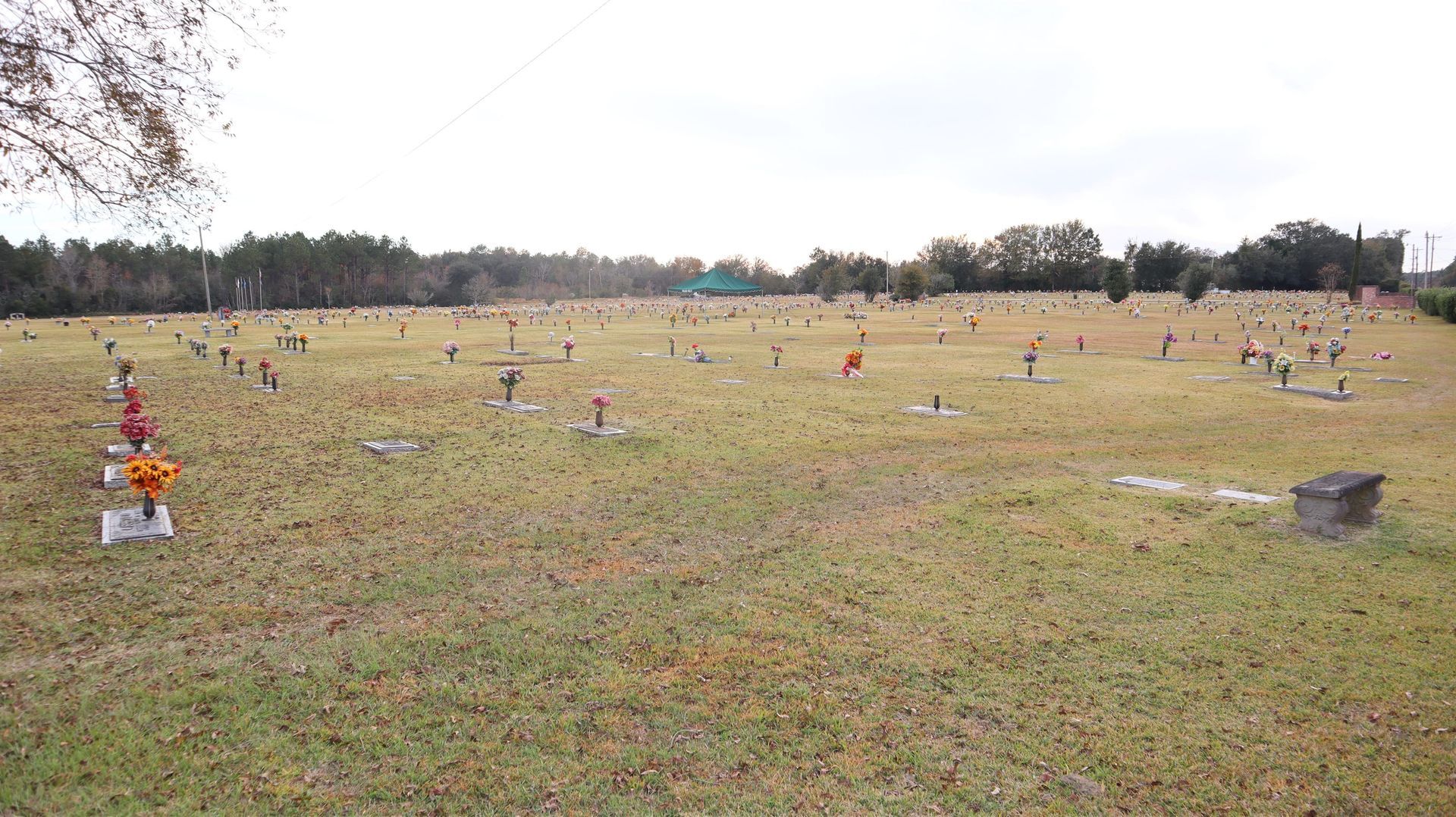 A wide, grassy cemetery field scattered with small, flat headstones under an overcast sky.