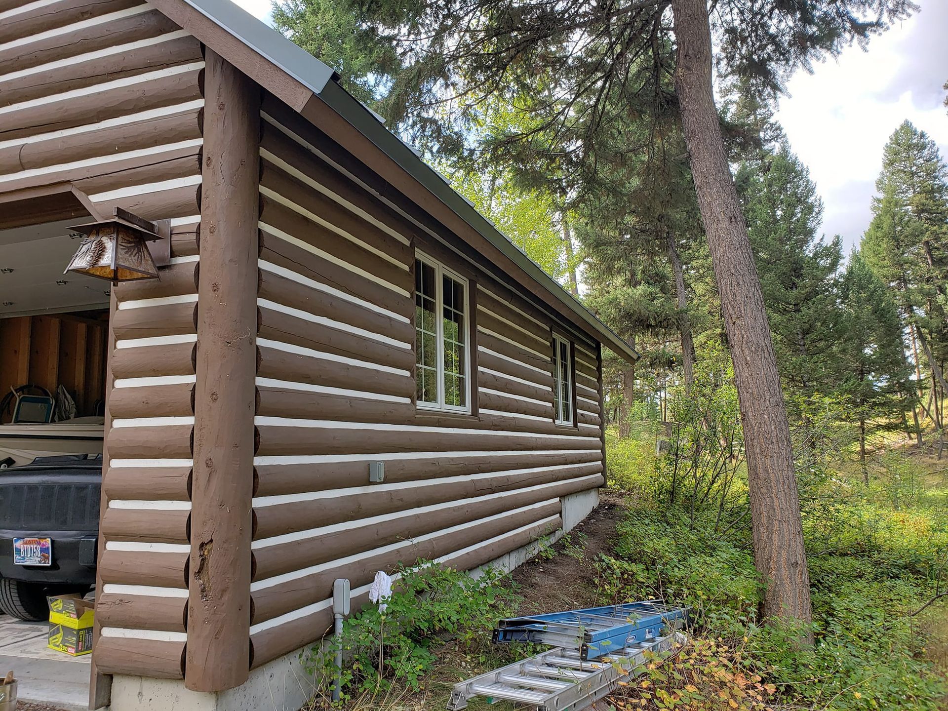 Log cabin with brown siding, two windows, and a nearby tree.