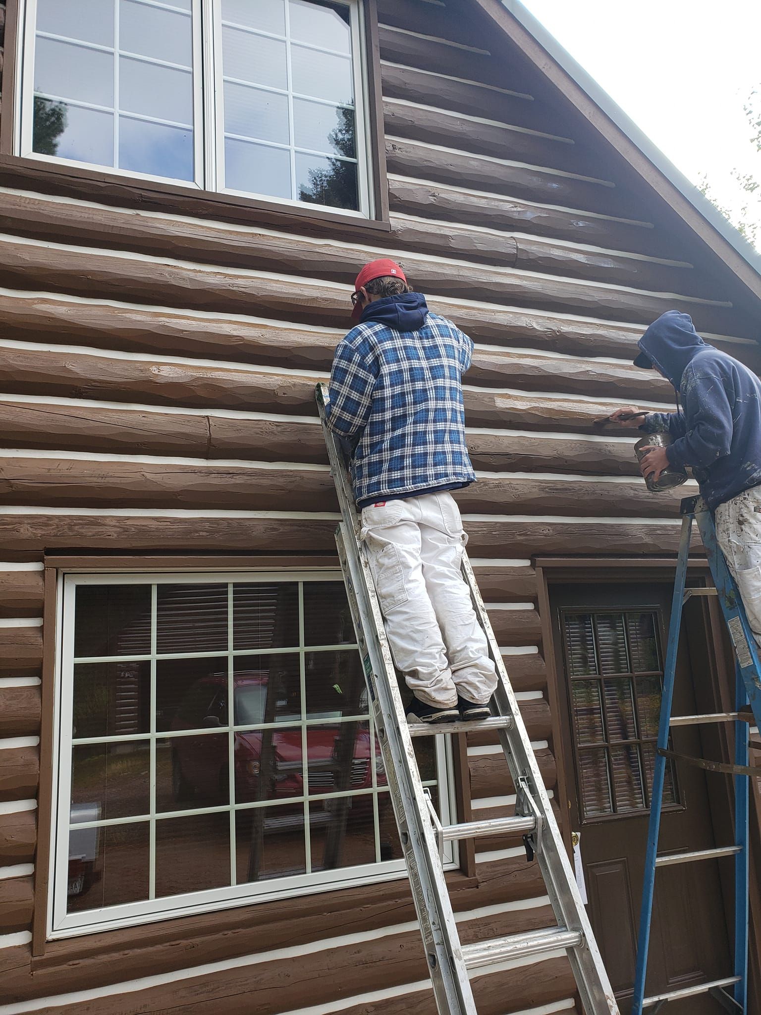 Two men are painting the side of a log cabin
