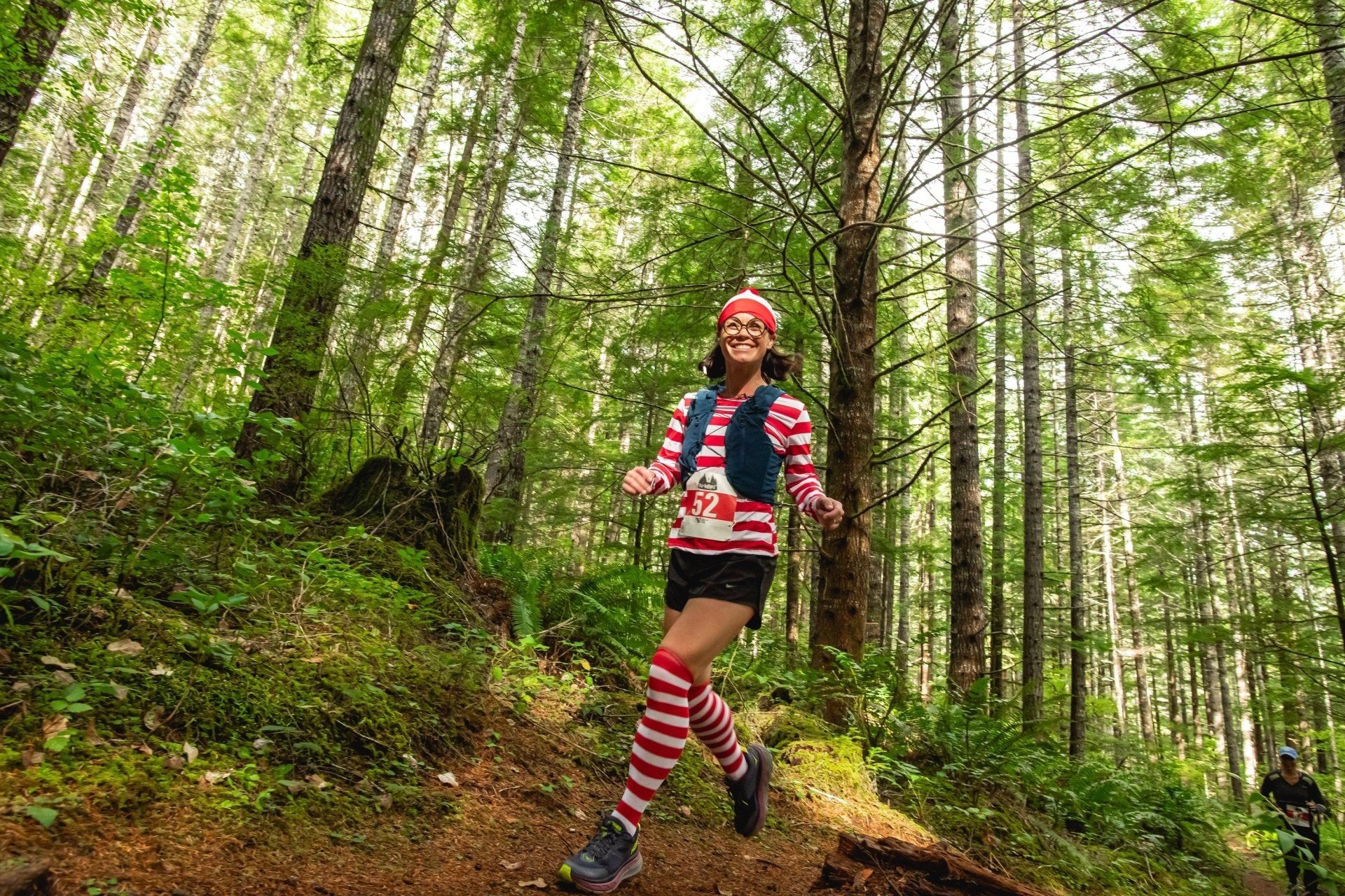 A woman is running through a forest wearing striped socks and a santa hat.