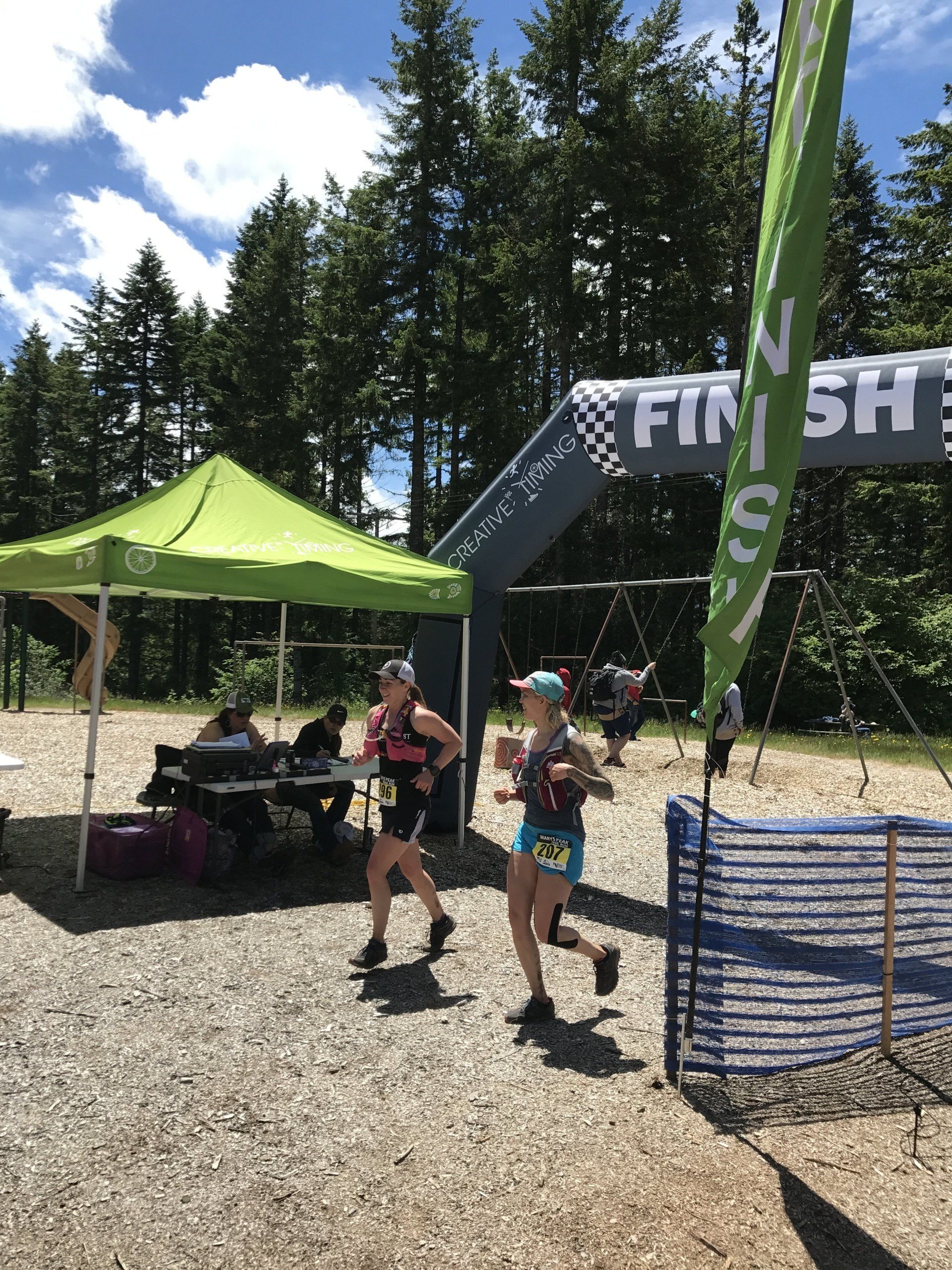 Two women are running in front of a finish line banner.