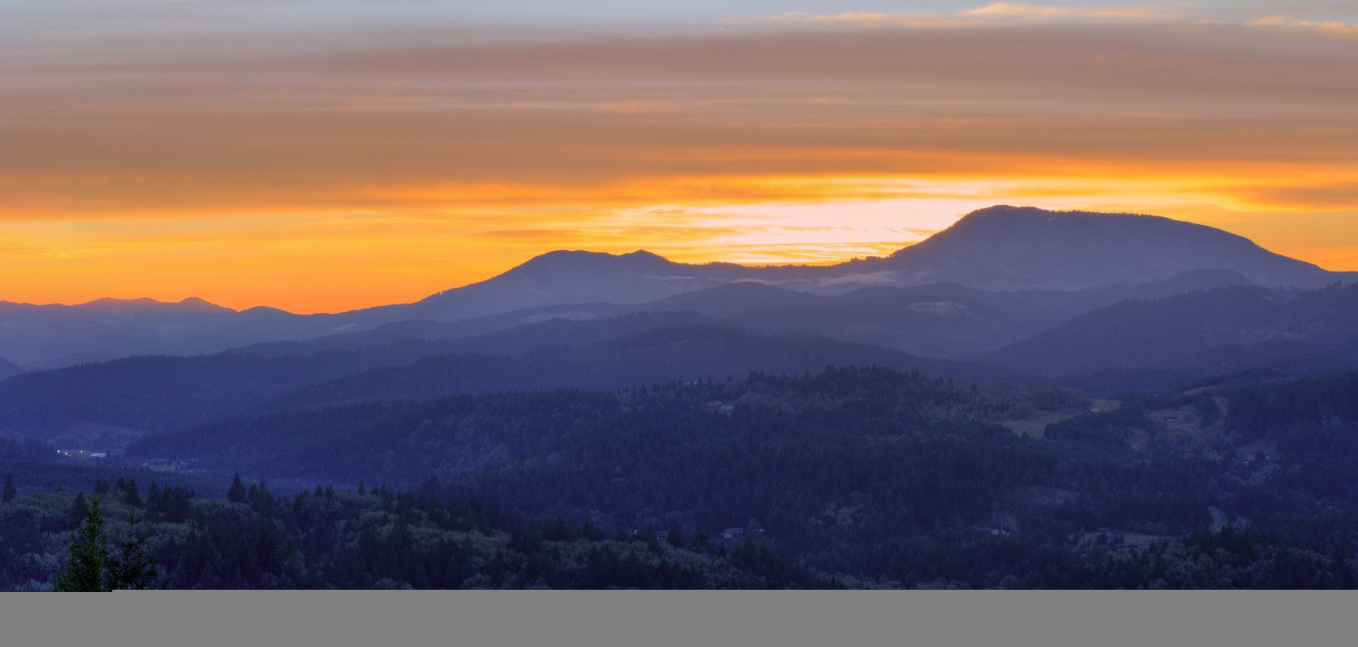 A sunset over a mountain range with trees in the foreground.