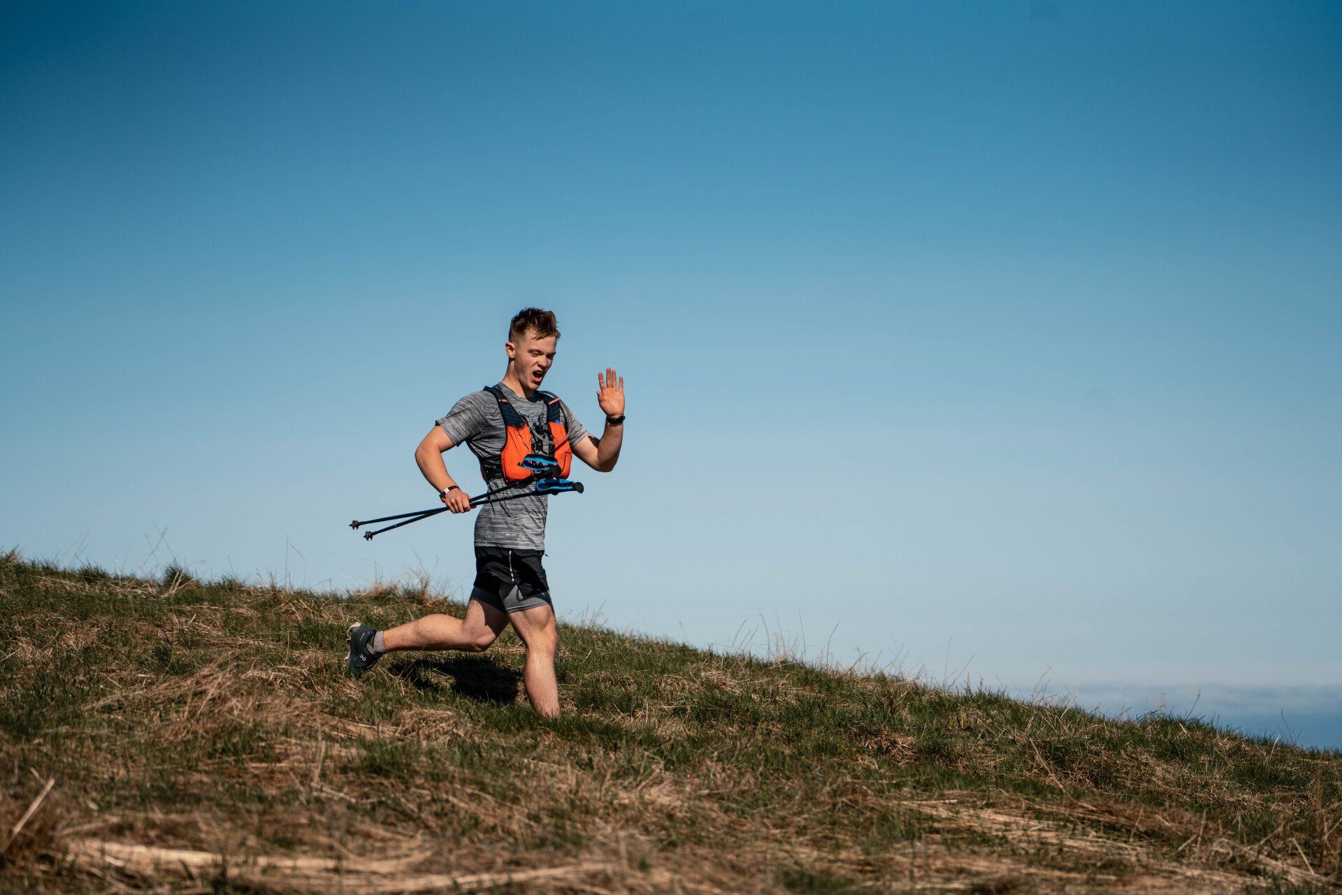 A man is running up a hill with a backpack and walking poles.