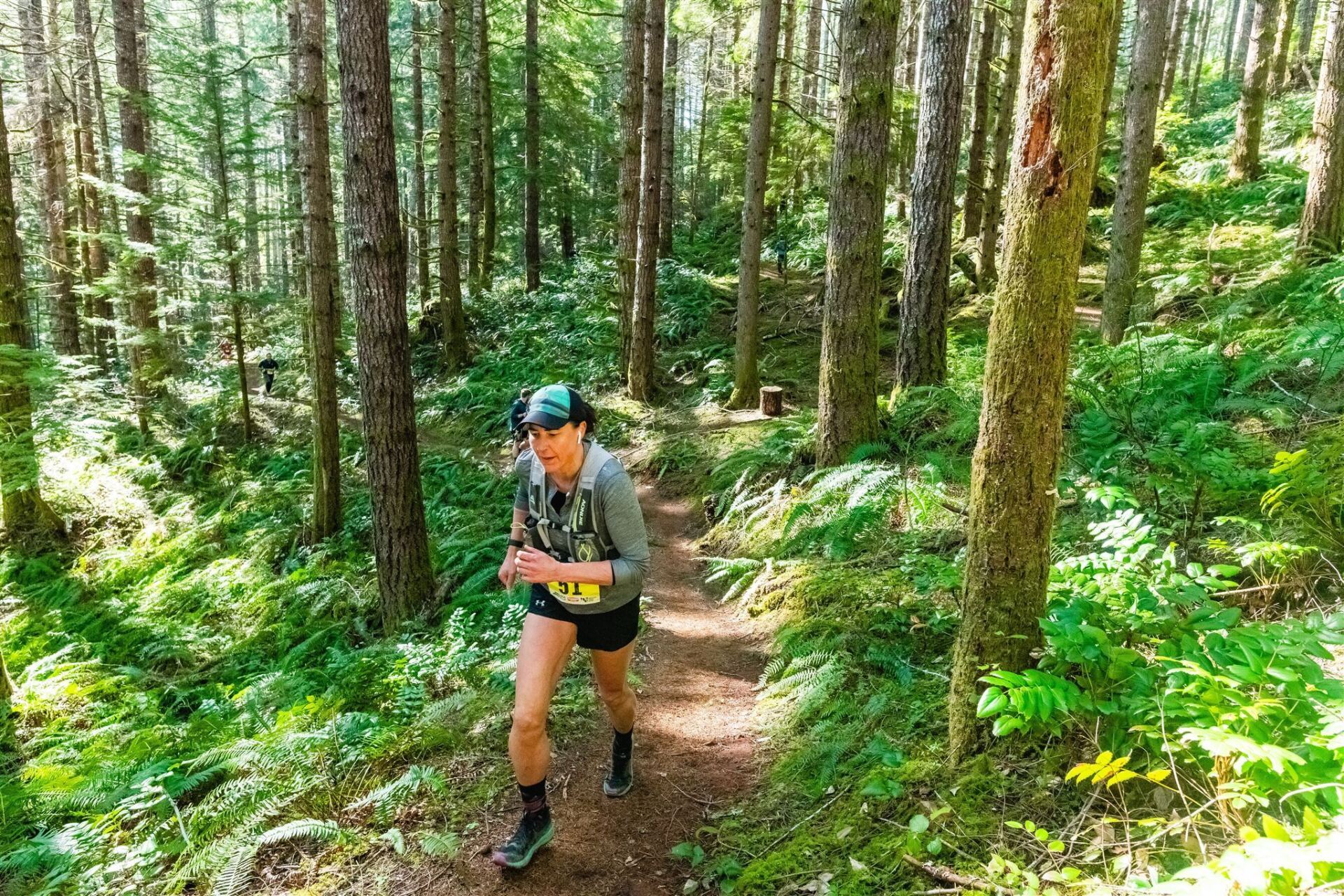 A woman is running down a trail in the woods.