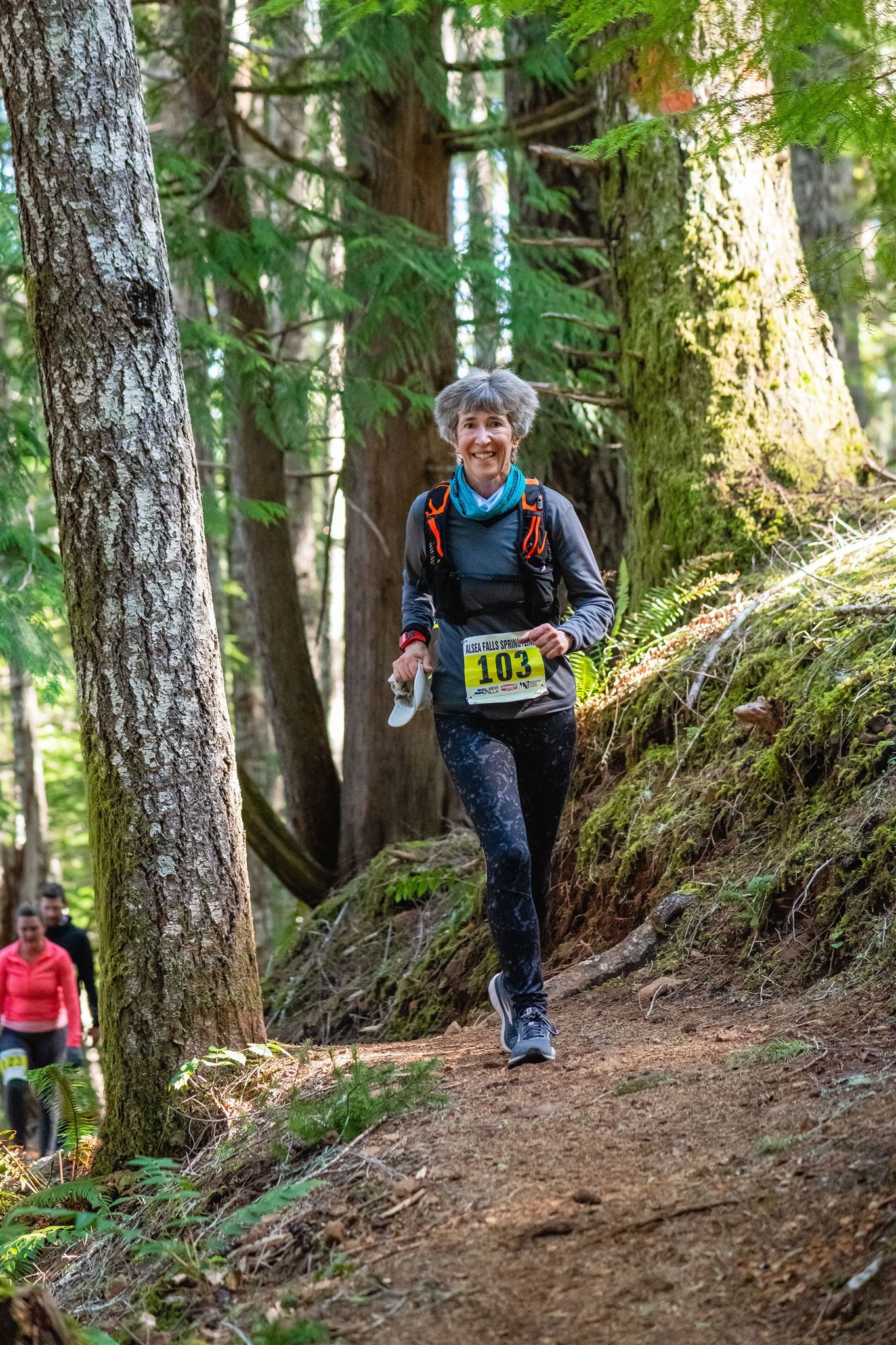 A woman is walking down a trail in the woods.