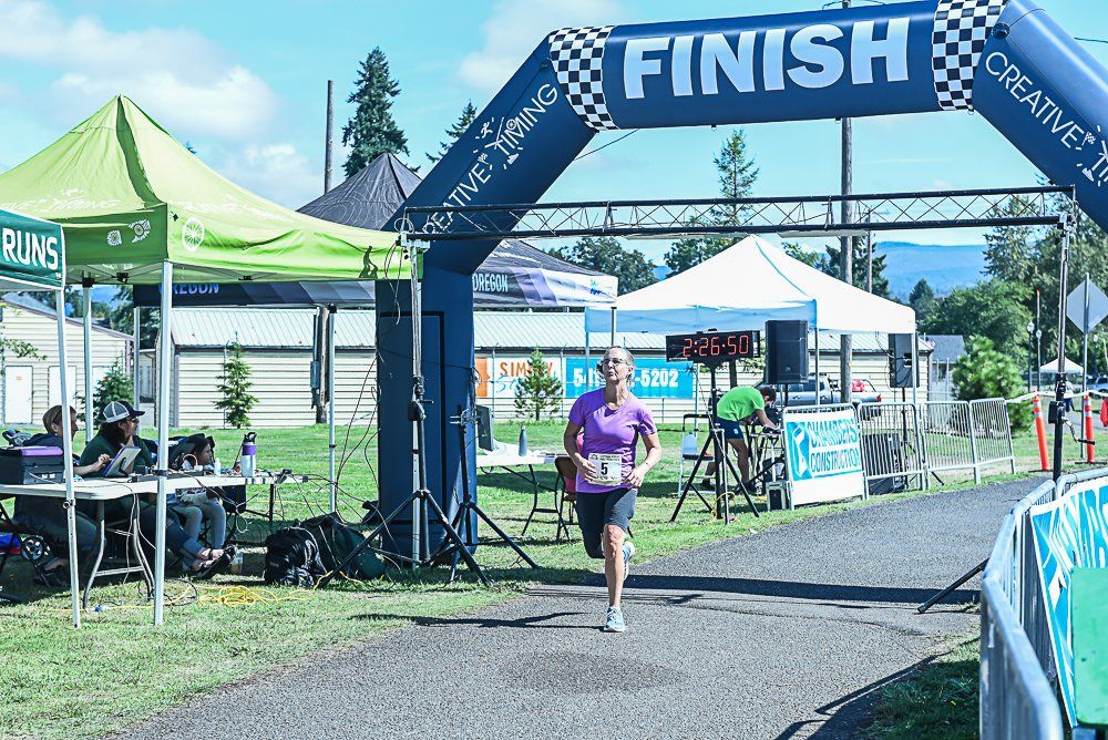 A woman is running through a finish line arch.