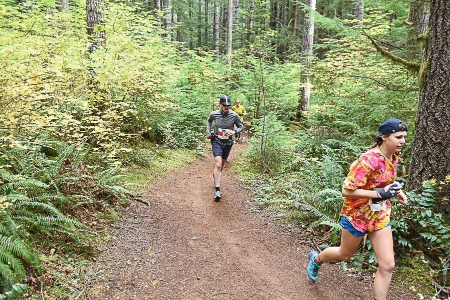 A man and a woman are running on a trail in the woods.