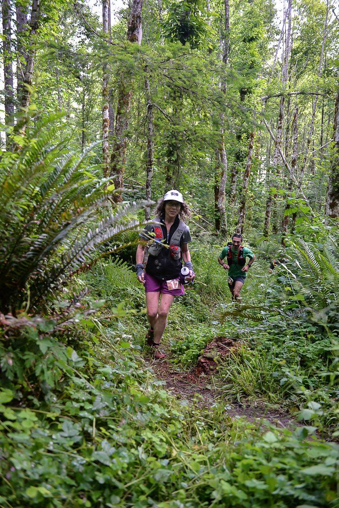 A man and a woman are running through a lush green forest.