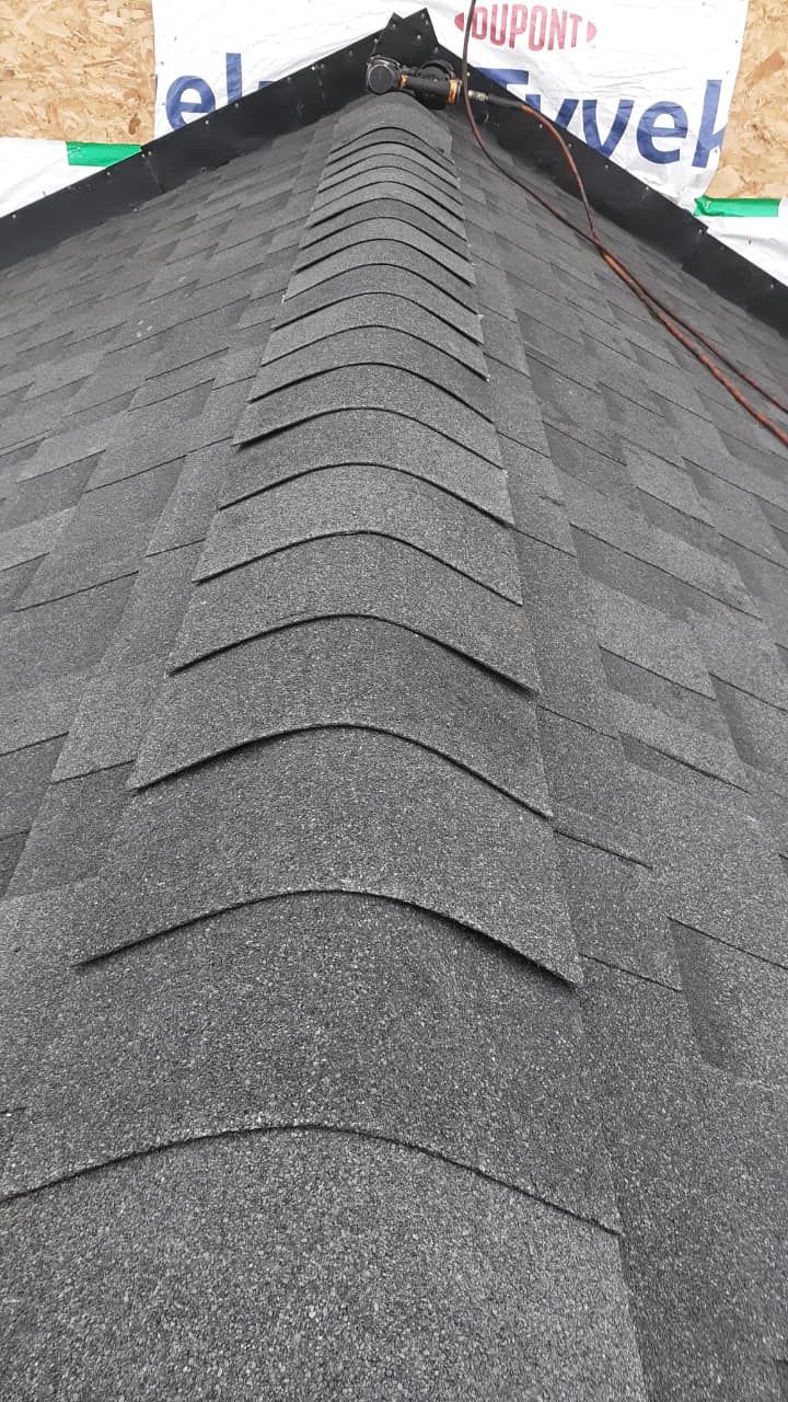 Dark gray asphalt shingles on a roof peak. The shingles are in rows, and a brown wire runs along the peak.