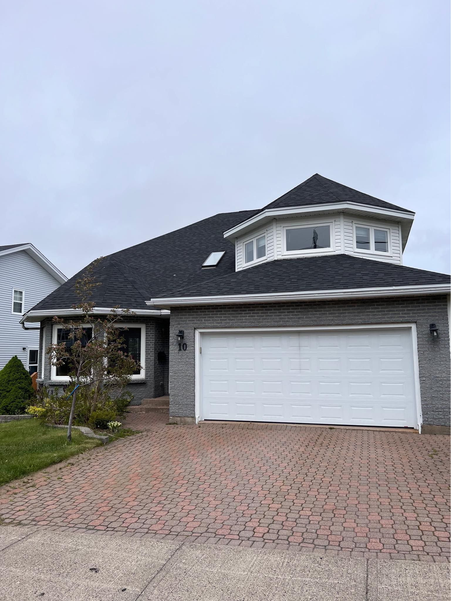 House with gray brick siding, white garage door, and a uniquely shaped roof with a smaller, octagonal structure on top.