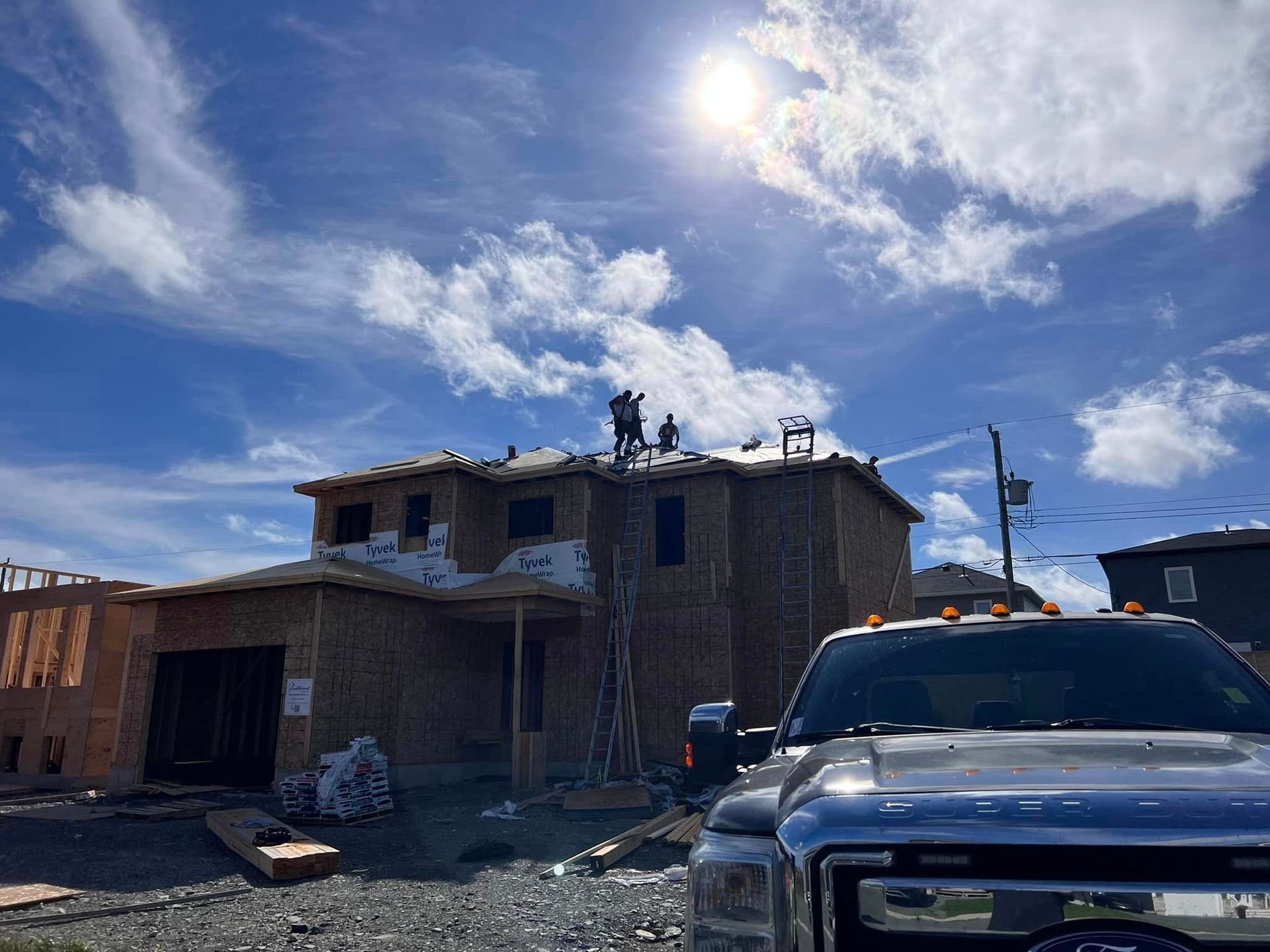 Construction workers on a house roof under a bright sun. New house framed and partly covered with siding.