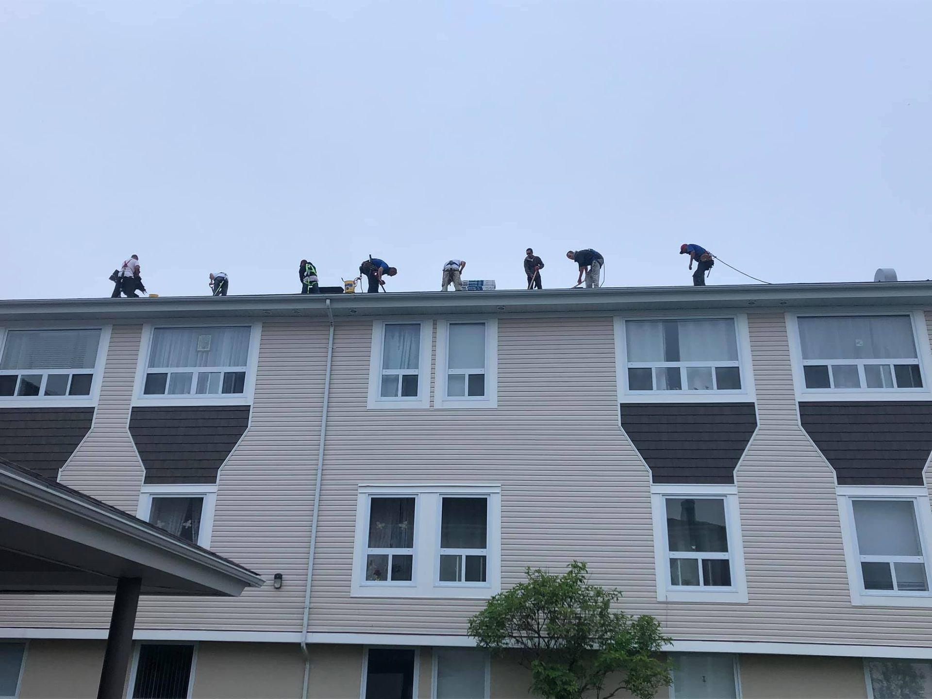 Workers on a building roof, possibly repairing it. They are silhouetted against a cloudy sky.