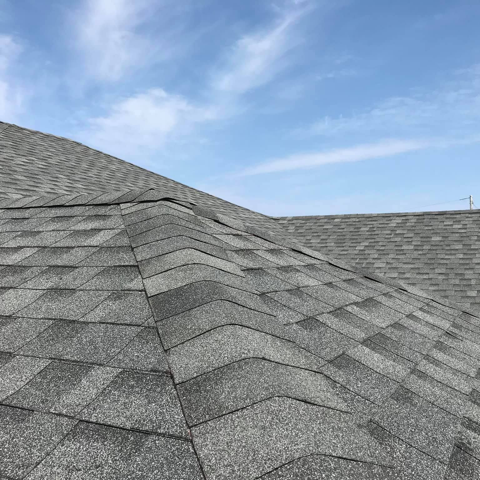 Gray asphalt shingle roof against a blue sky with scattered clouds. Close-up view.