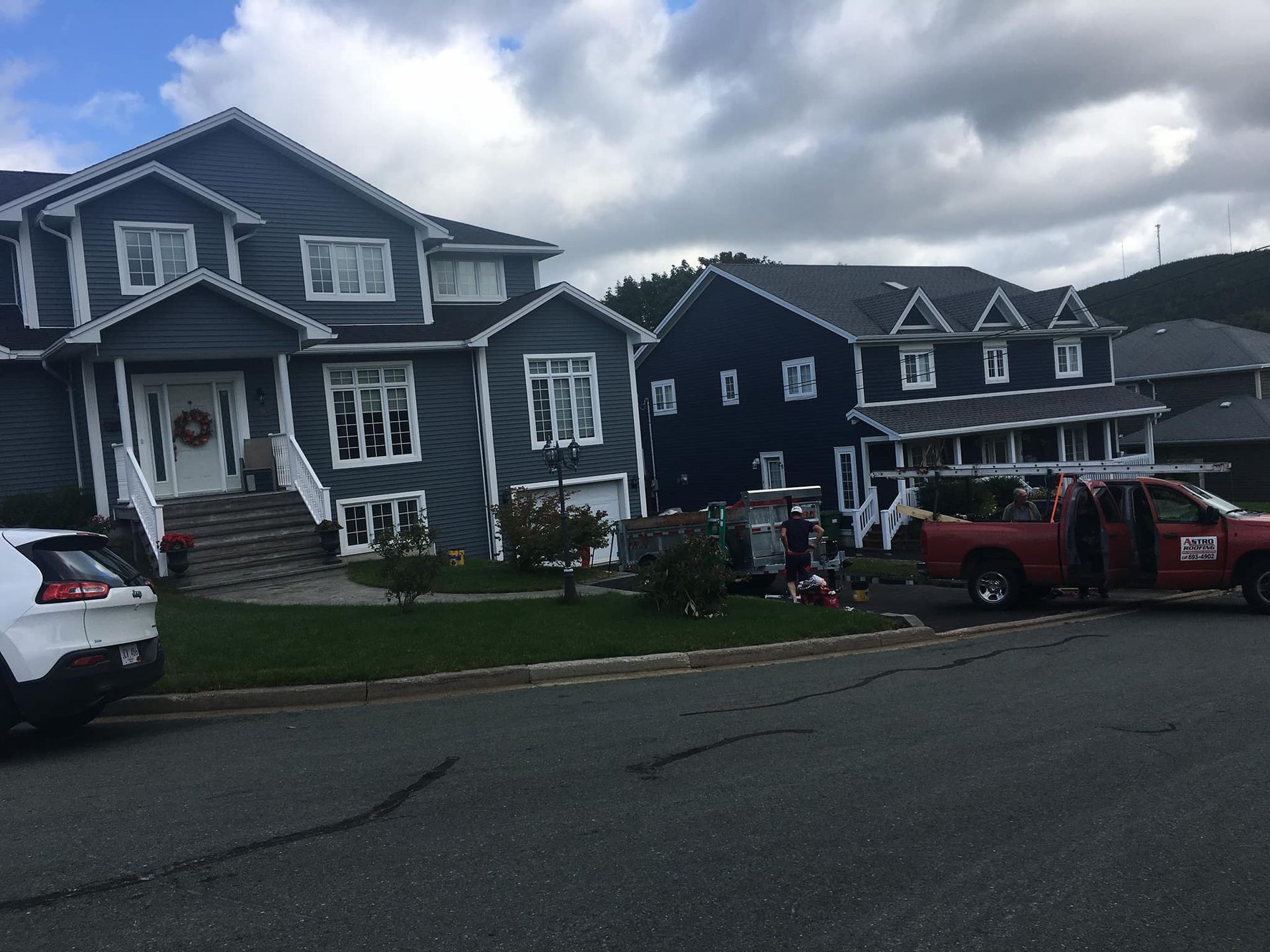 Two-story houses on a street. A red truck parked in front with people near it and a white SUV to the left.