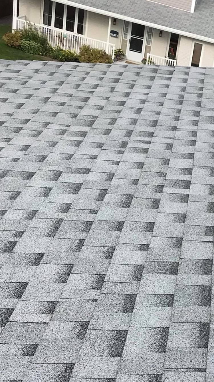 Gray and white asphalt shingle roof.  The roof is a textured surface with a house in the background.