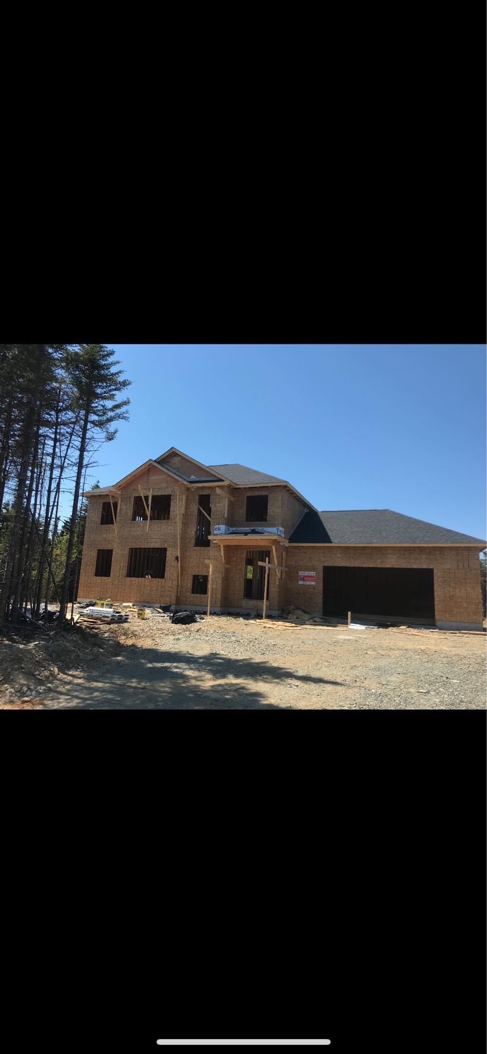 A two-story house under construction on a sunny day. Framing and unfinished siding are visible.