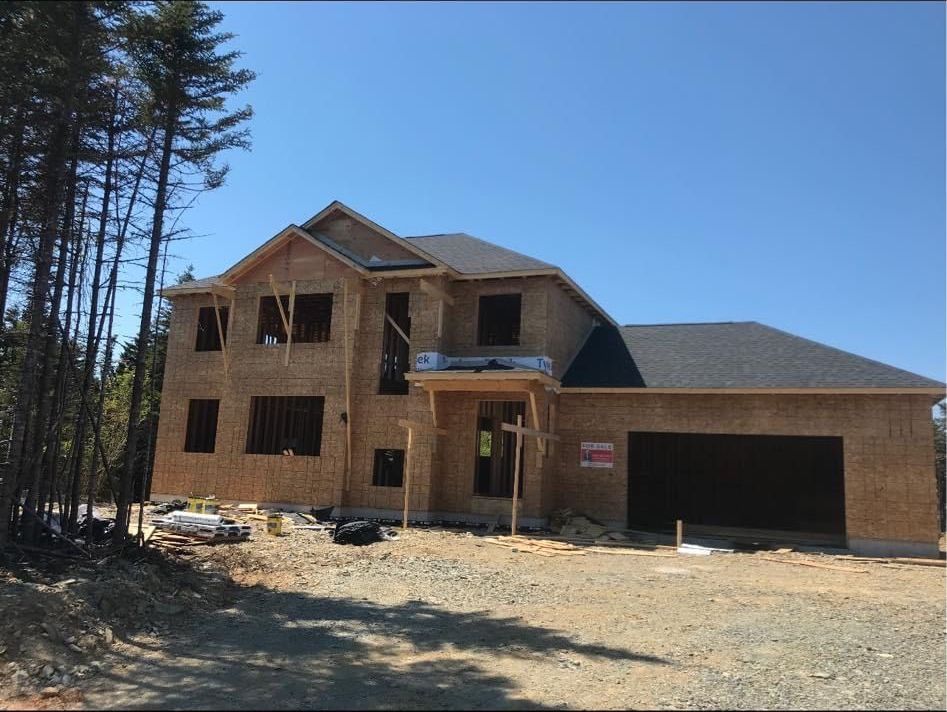 New two-story house under construction on a gravel lot, framed with wood, under a clear blue sky.