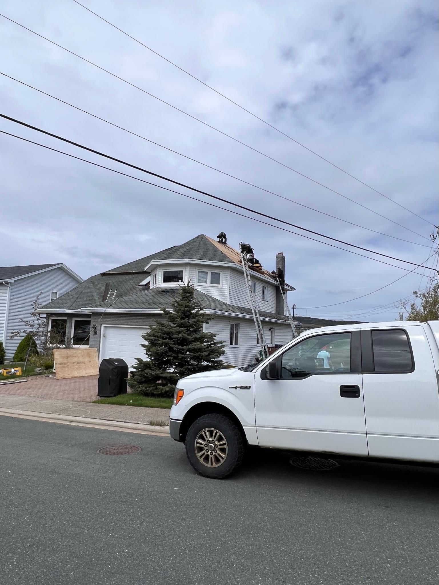 White truck parked in front of a house with workers on the roof. Cloudy sky.