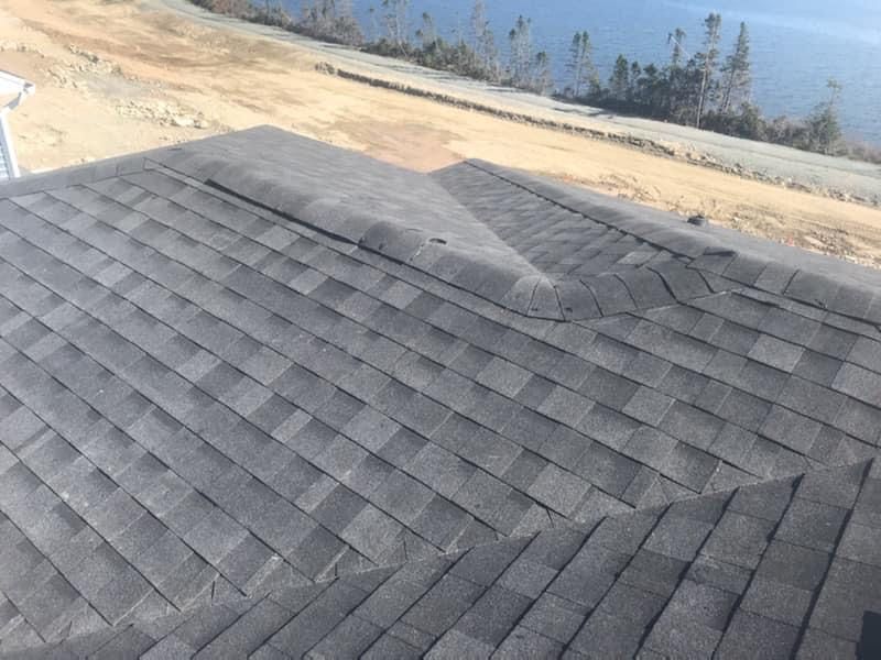 Gray asphalt shingle roof with a damaged section at an angled corner, overlooking a body of water.
