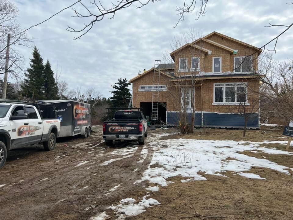 Construction site with a two-story house under renovation. Trucks and a trailer parked on a muddy lot, with snow patches.