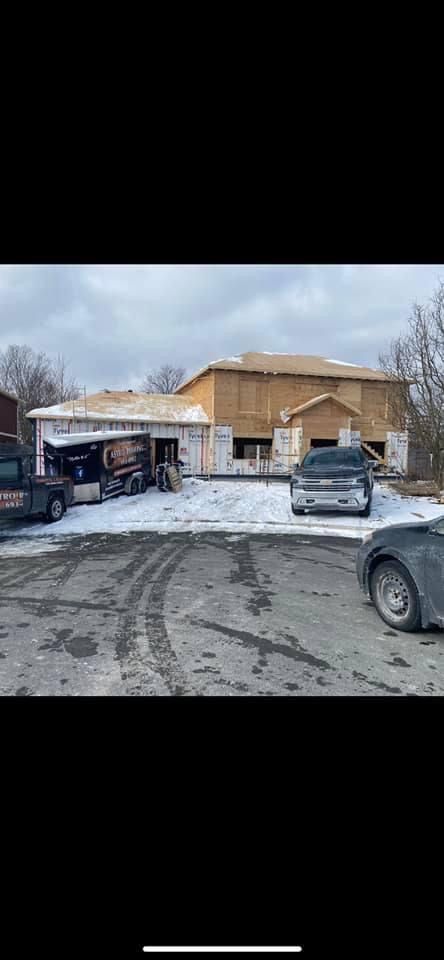 A building under construction with a partly snowy lot and a few vehicles parked on the side.