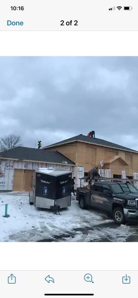 Construction site with a partially built building, a truck, and a trailer on a snowy ground under a cloudy sky.