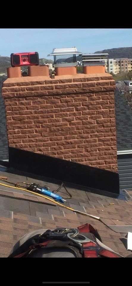 Brick chimney on a rooftop, with a red radio and metal vents on top. Tools and safety gear are present on the roof.