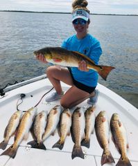 A woman is kneeling on a boat holding a large fish.