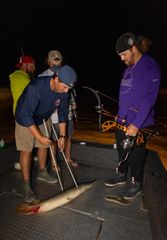 A group of men are fishing on a boat at night.