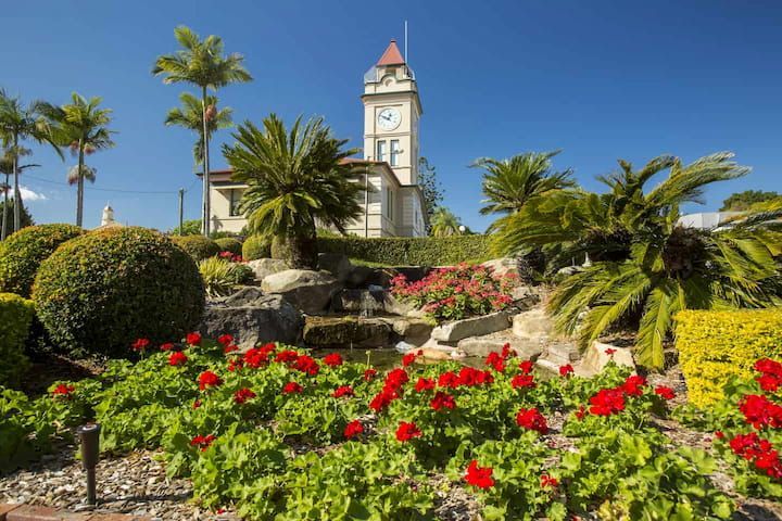 A Clock Tower Is Surrounded by Flowers and Trees in A Garden — Cooloola Tile Company in Gympie, QLD