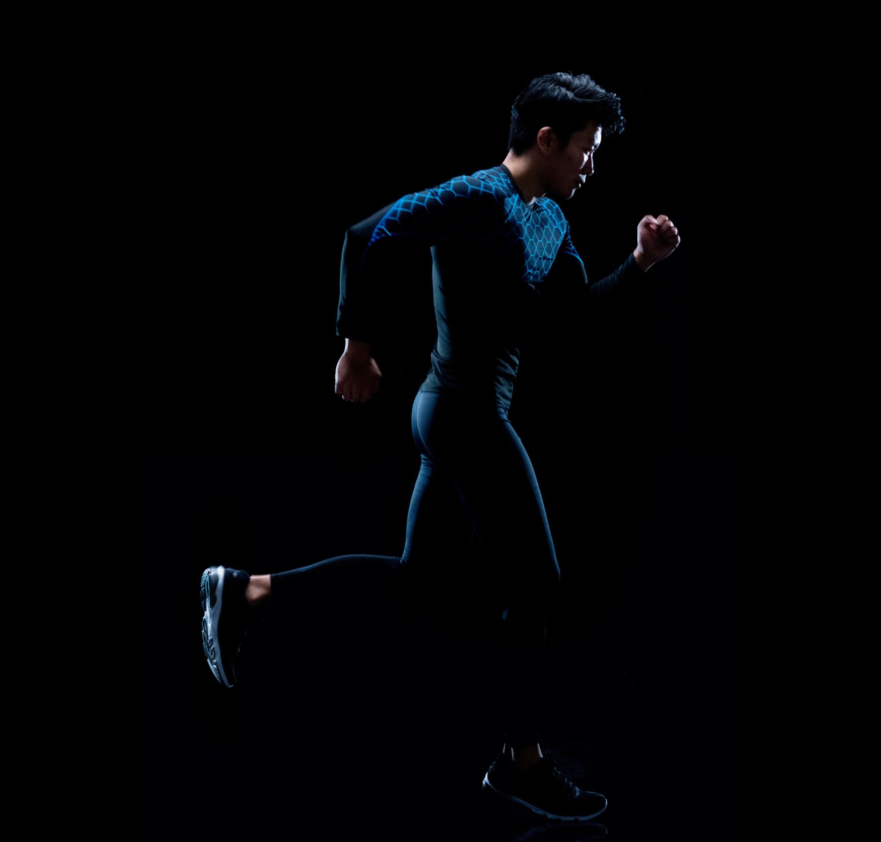 Runner in dark athletic wear, side view, silhouetted against black background. Runner in dark athletic wear, side view, silhouetted against black background.