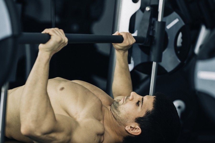 Man lying on a bench, lifting a barbell in a gym.