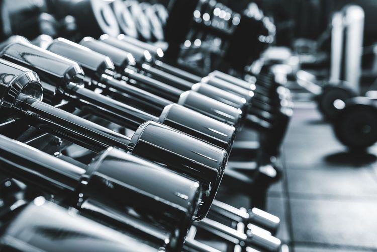 Row of dumbbells on a rack in a gym, with other workout equipment in the blurred background.