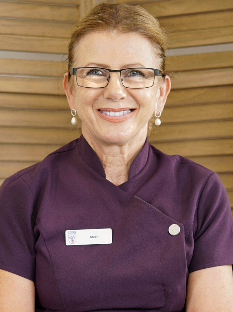 A woman wearing glasses and a purple shirt smiles for the camera